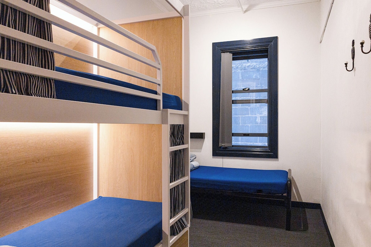 A bunk bed room with a window, a wooden wardrobe, and a small table.