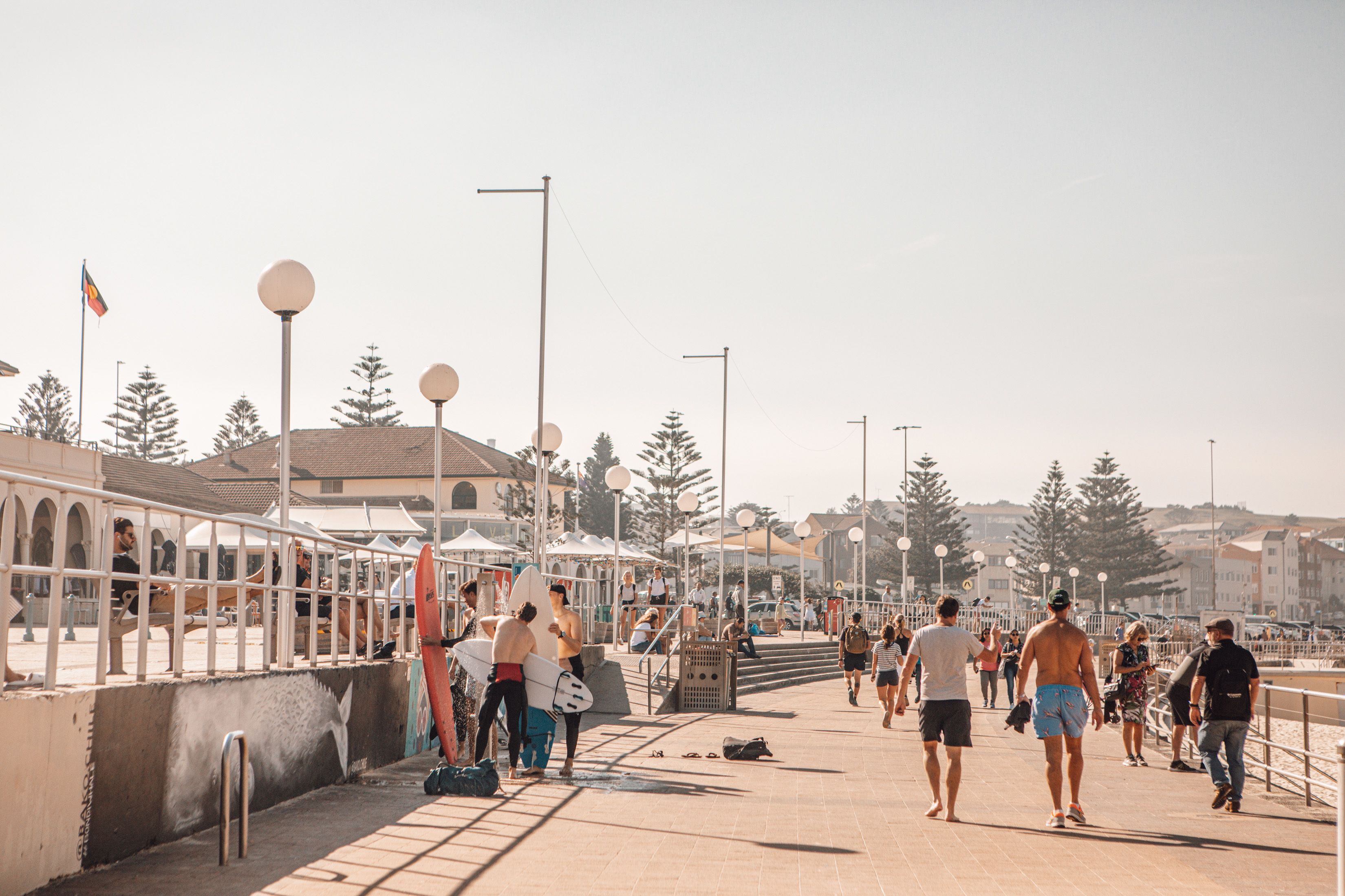 A coastal promenade with a walkway, beach umbrellas, and people walking.