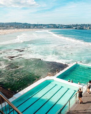 Une piscine à l’eau d’un bleu cristallin, une plage et, au loin, une vue sur la ville.