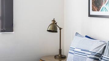 A bed with striped bedding, a round wooden nightstand, and a vintage-style desk lamp.