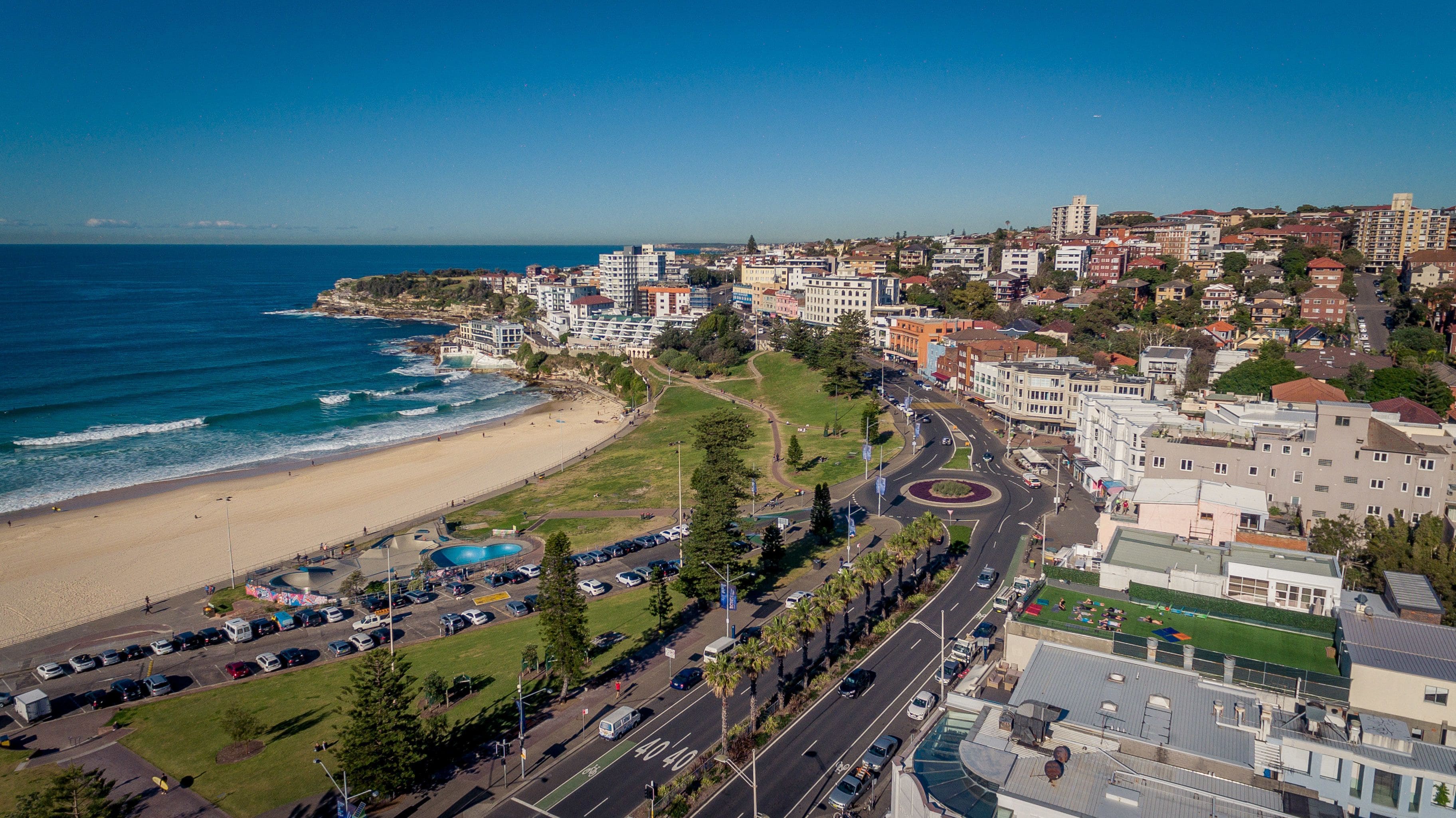 An aerial view of a coastal city with a beach, roads, and buildings.