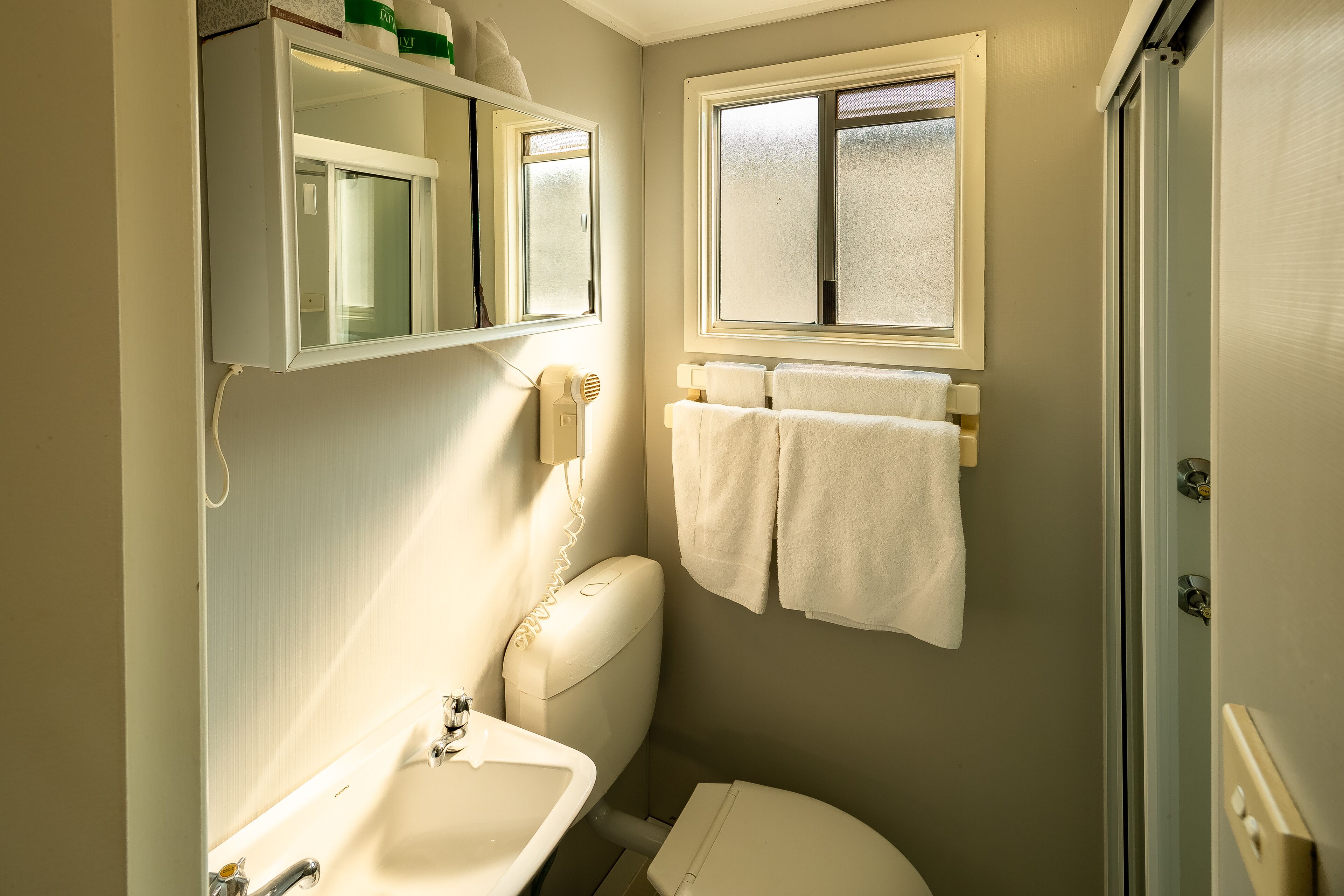 A compact bathroom with a toilet, sink, and a window above the toilet.