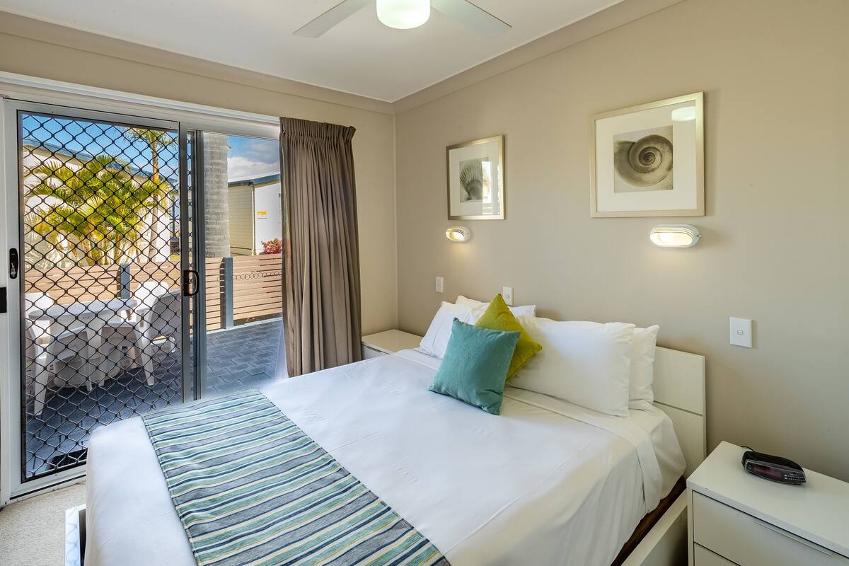 Une chambre d’hôtel avec un lit, une table de chevet, un ventilateur de plafond et une vue sur l’extérieur, accessible par une porte-fenêtre coulissante.