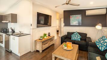 A modern kitchen with white cabinetry, a built-in oven, and a dining area with a wooden table and black sofa.