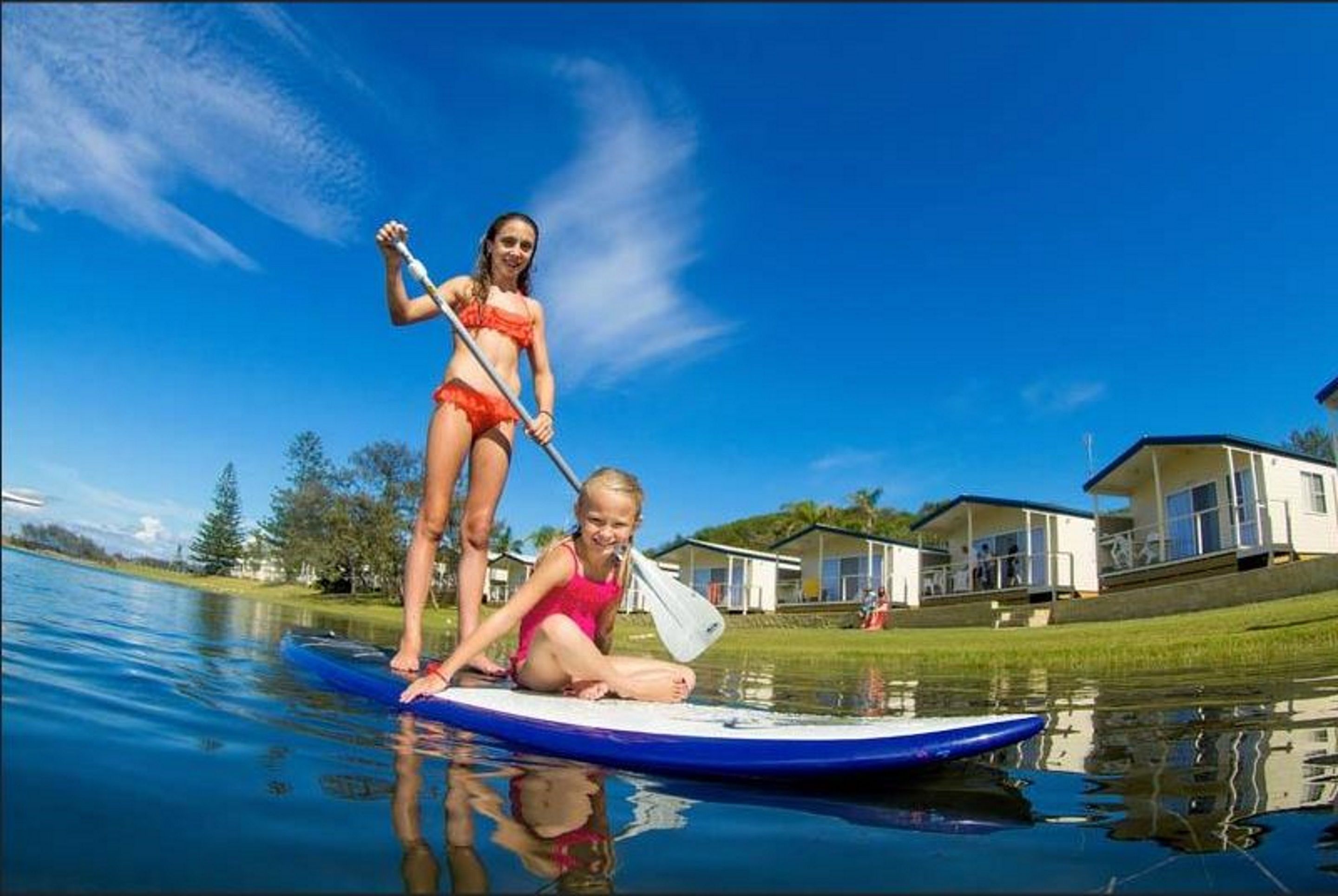 Two people on a paddleboard in a calm body of water with houses in the background.