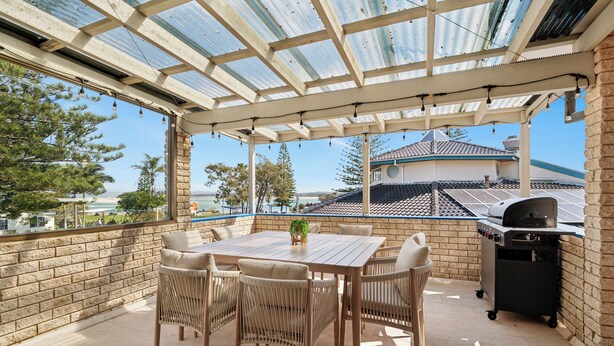 Un patio techado con mesa y sillas, una parrilla y vista al océano.