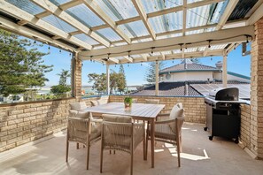 Un patio techado con mesa y sillas, una parrilla y vista al océano.