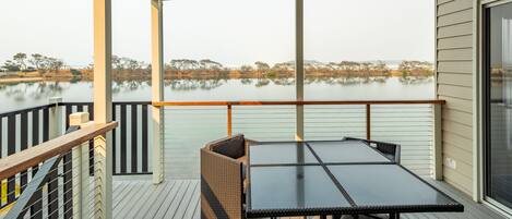 Una terraza con una mesa y sillas, con vista a un cuerpo de agua tranquilo y árboles.