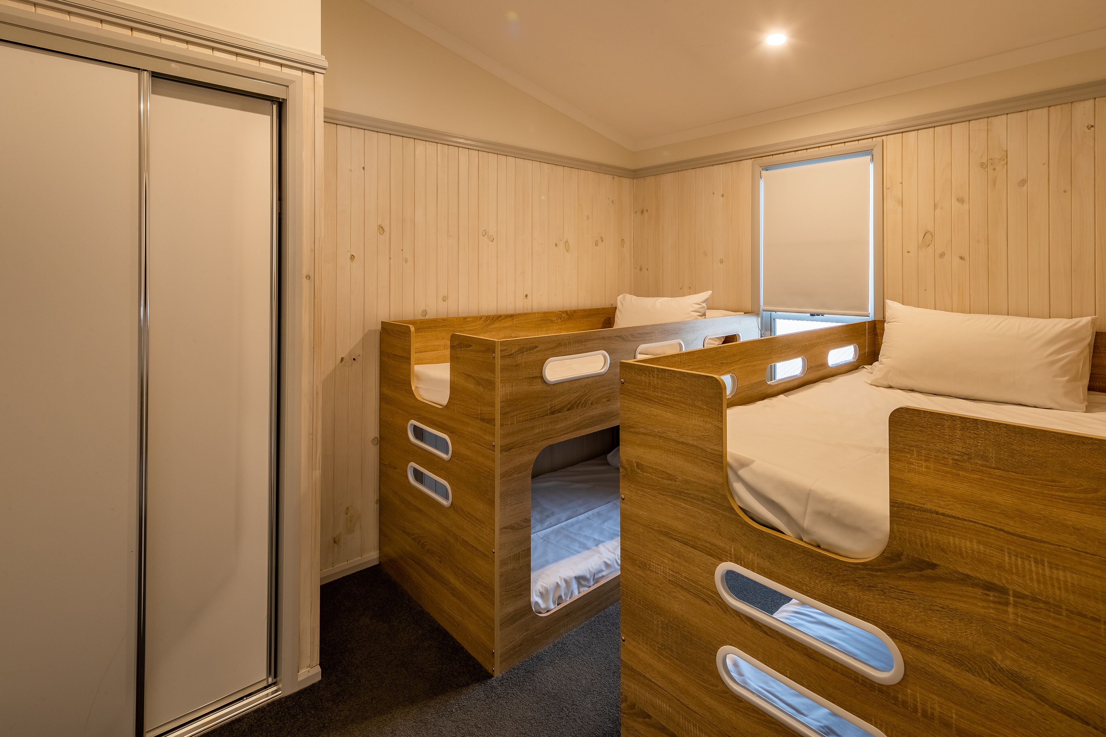 Une chambre à coucher avec un lit superposé, une armoire en bois et une fenêtre avec des stores.