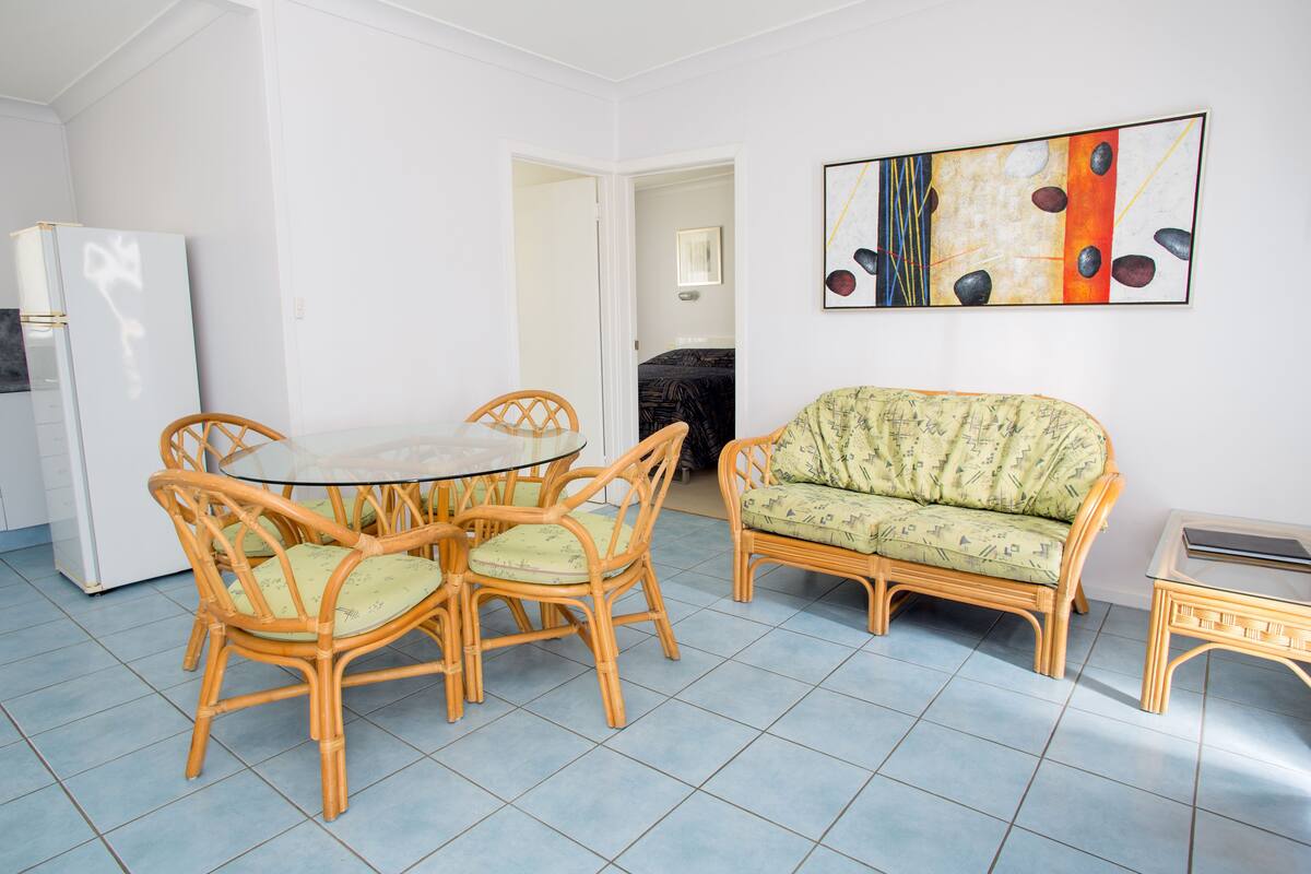 Une pièce comprenant une table à manger entourée de chaises en osier, un canapé et un réfrigérateur.