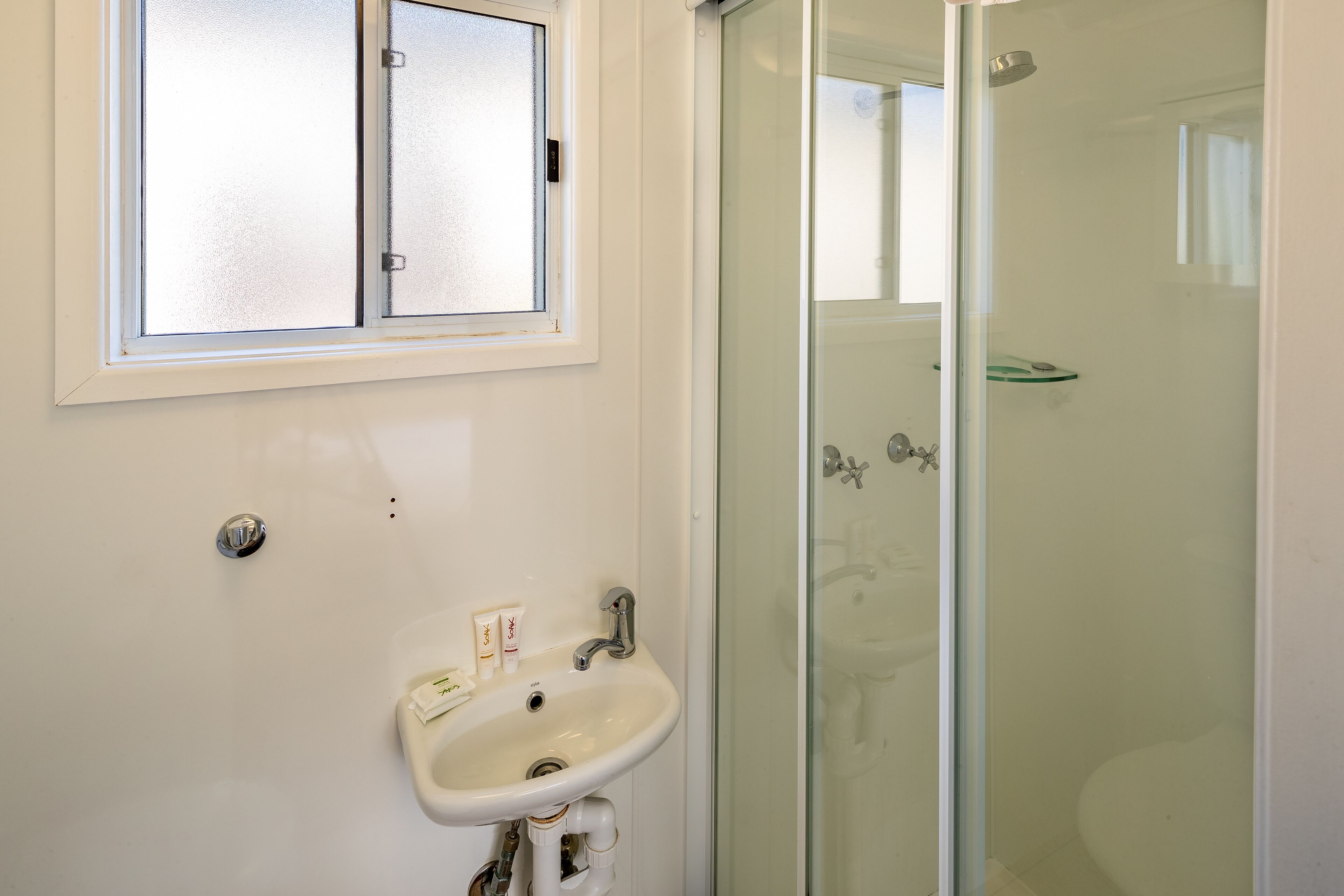 A bathroom with a white sink, a frosted window, and a glass shower enclosure.