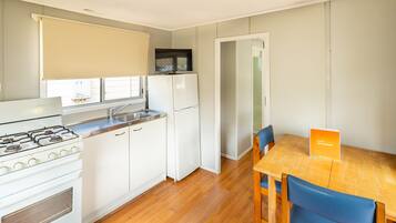 Cocina compacta con estufa, lavamanos y refrigerador, una mesa de comedor con sillas y vista a la calle a través de una ventana.