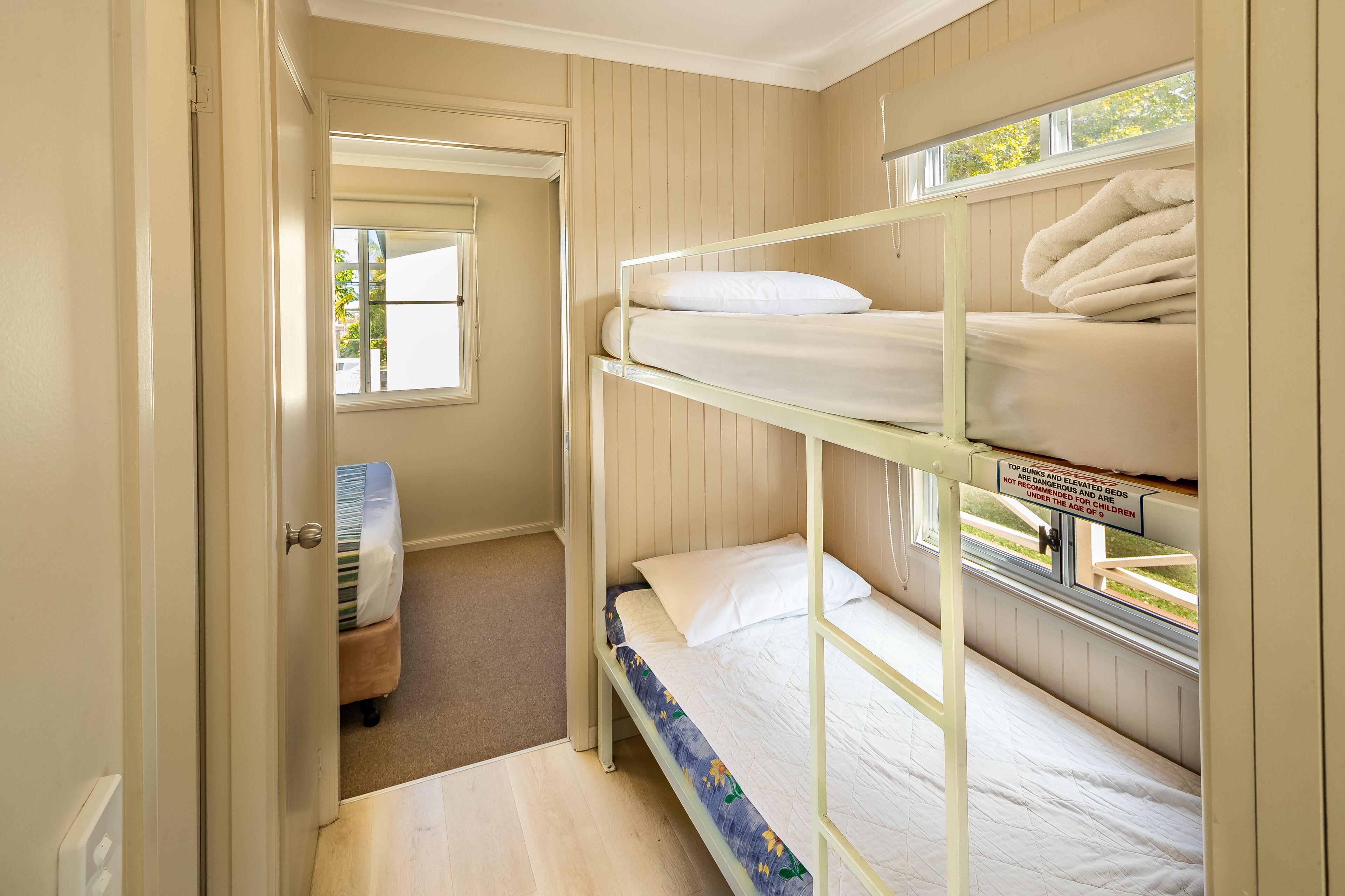 A bunk bed room with a window, a door, and a small stool.
