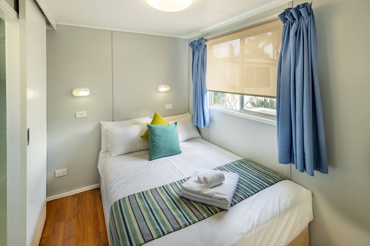 Un lit bien fait, avec des draps blancs, un coussin à rayures et une serviette pliée posée sur un couvre-lit à rayures.