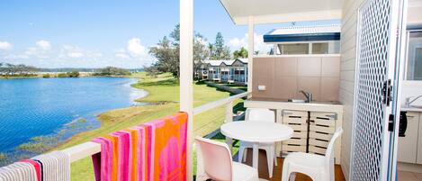 A balcony with a view of a lake, a small table with chairs, and a kitchen area.