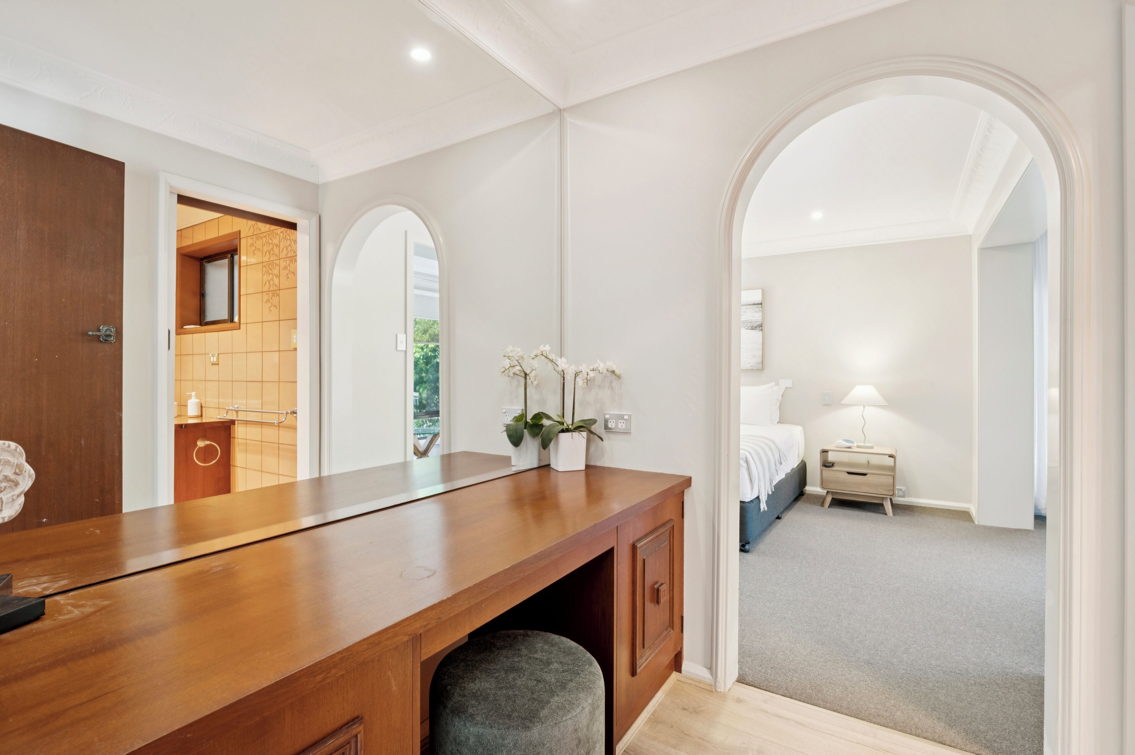 A modern bedroom with a wooden vanity, a small window, and a nightstand with a lamp.