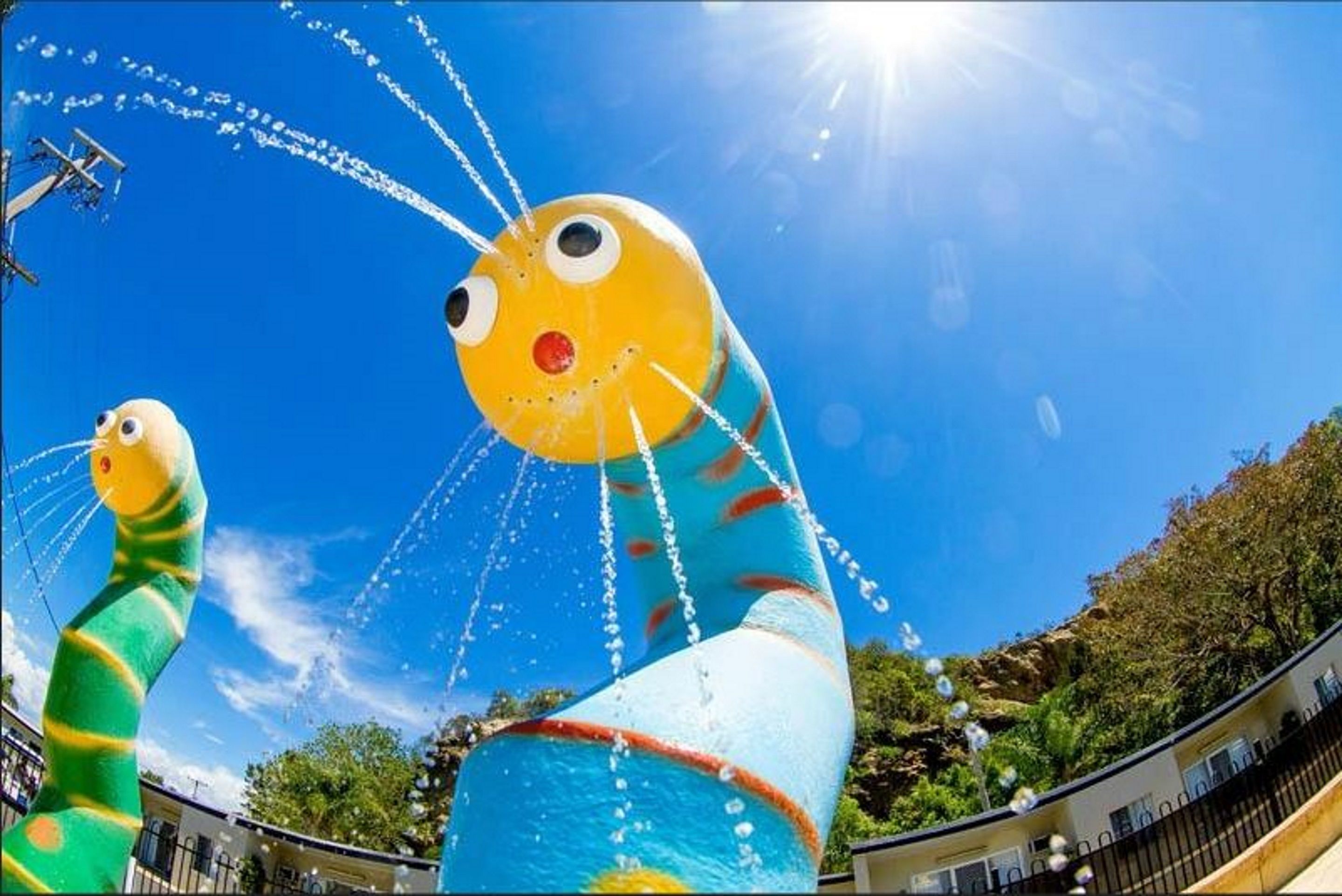 Une grande sculpture gonflable représentant une créature jaune avec un nez rouge et un corps bleu, placée sur fond de ciel bleu clair.