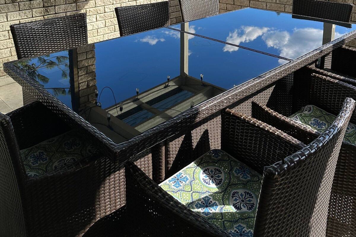 Un espace extérieur abrité, aménagé pour les repas, avec une table à plateau de verre et des chaises en osier, offrant une vue sur un paysage pittoresque.