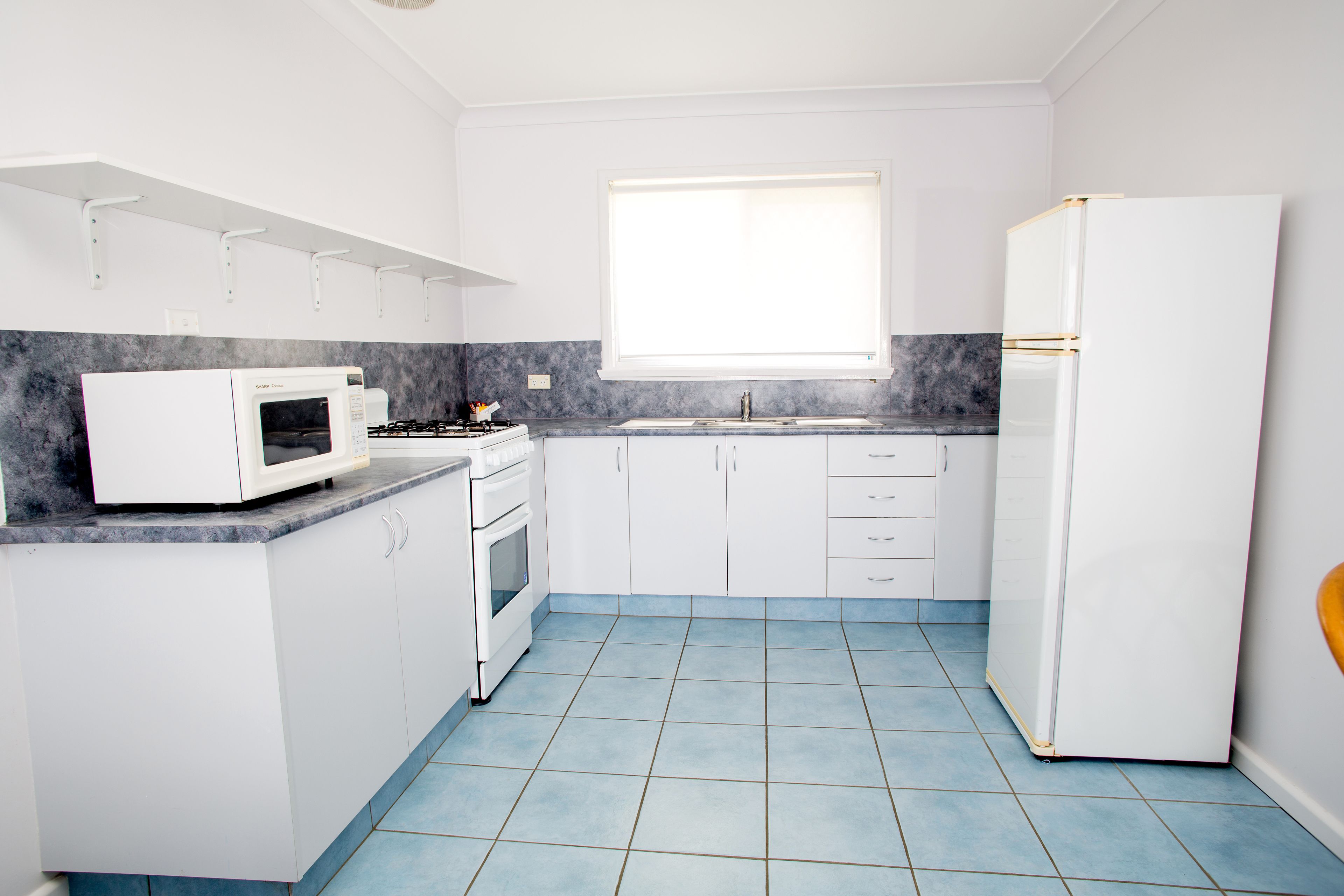 A compact kitchen with white cabinets, a white refrigerator, a microwave, and a stove.