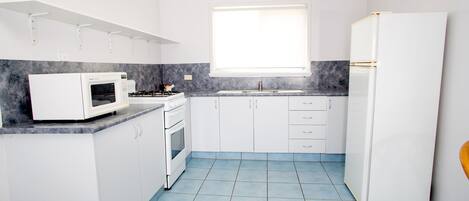 A compact kitchen with white cabinets, a white refrigerator, a microwave, and a stove.