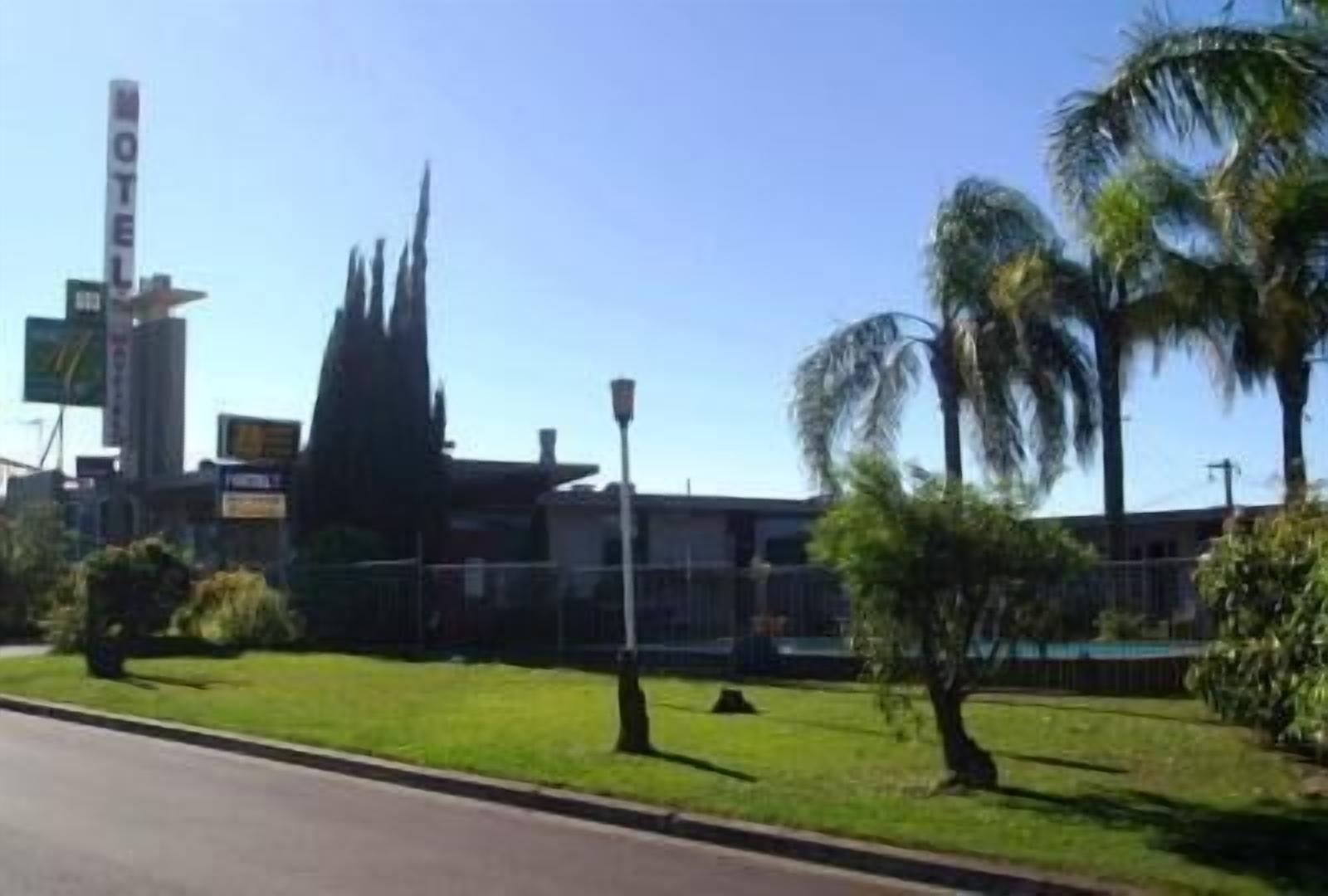 A motel with a tall sign, a building with a pointed roof, and palm trees in the foreground.