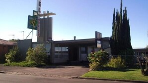 Un motel con un letrero vertical llamativo, un pequeño estacionamiento y un árbol alto en la entrada.