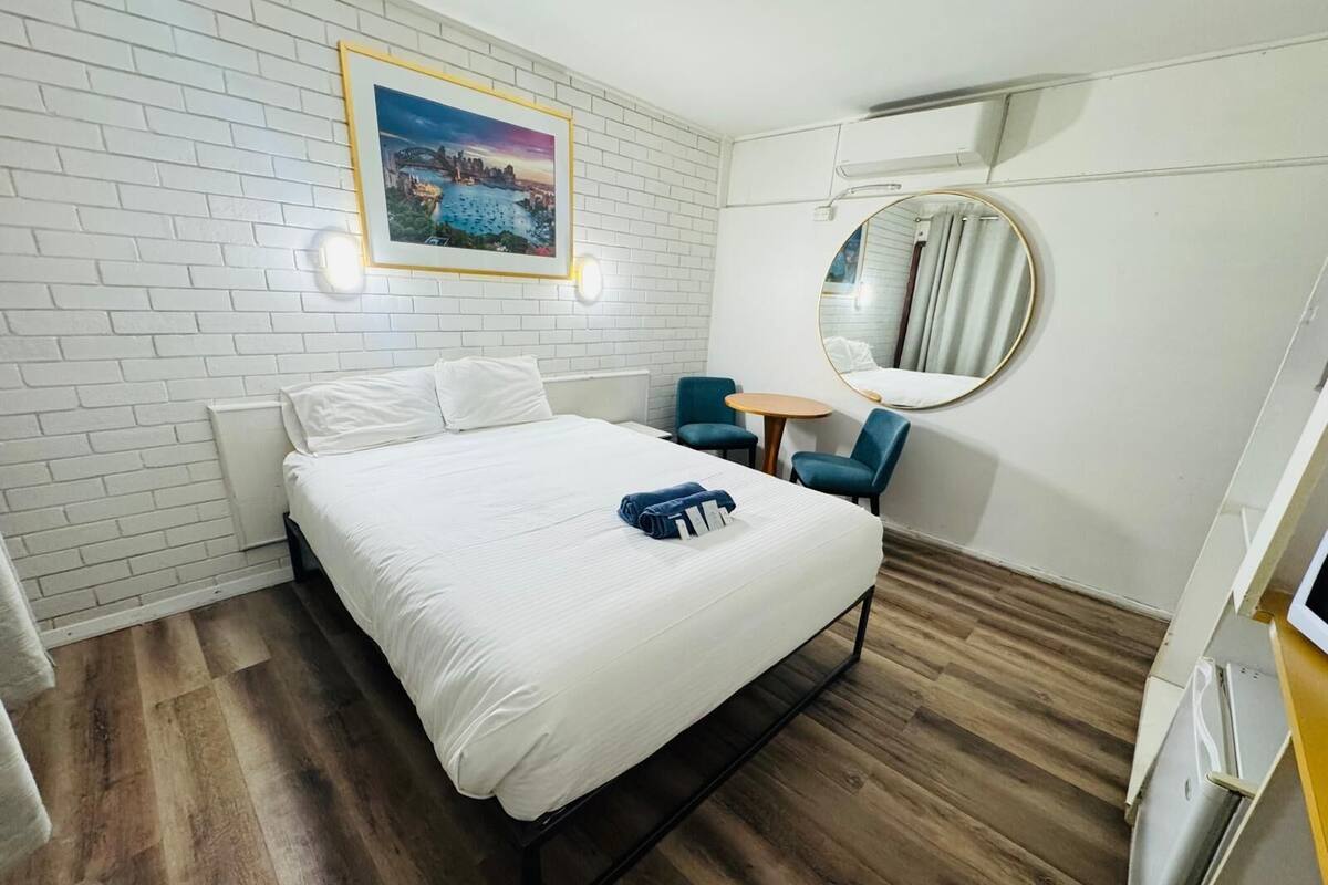 A hotel room with a bed, a round mirror, a small table, and a wall-mounted picture.