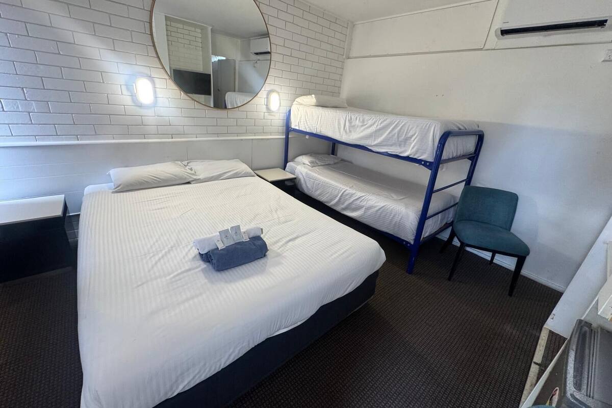 A room with two beds, a bunk bed, a chair, a mirror, and a small table.