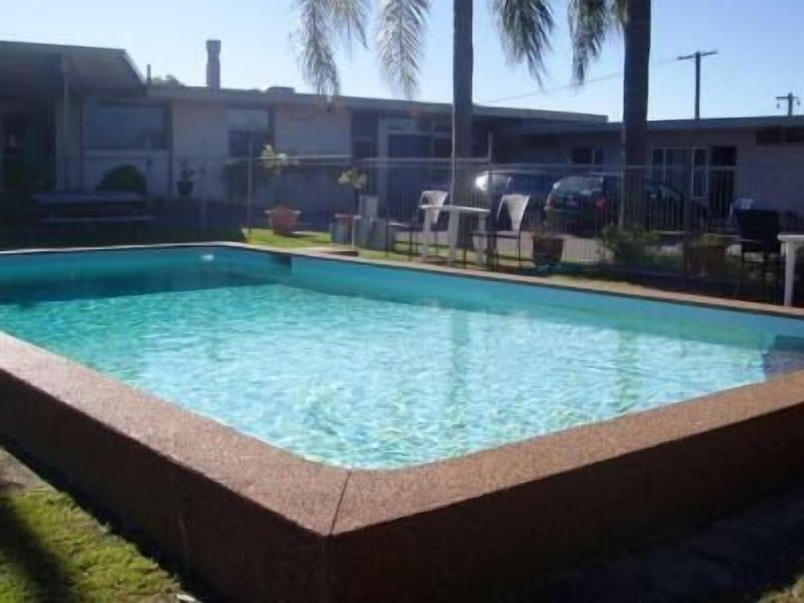 A rectangular swimming pool with clear blue water, surrounded by a grassy area and a fence.