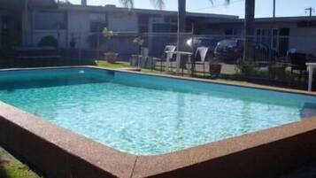A rectangular swimming pool with clear blue water, surrounded by a grassy area and a fence.
