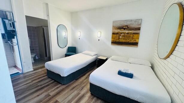 Habitación de hotel con dos camas, un espejo grande, un cuadro en la pared y suelo de madera.