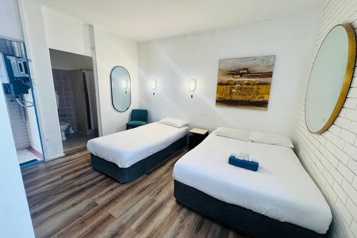 A hotel room with two beds, a large mirror, a painting on the wall, and a wooden floor.