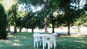 Juego de mesa y sillas de plástico blanco sobre una zona cubierta de césped, rodeado de árboles.