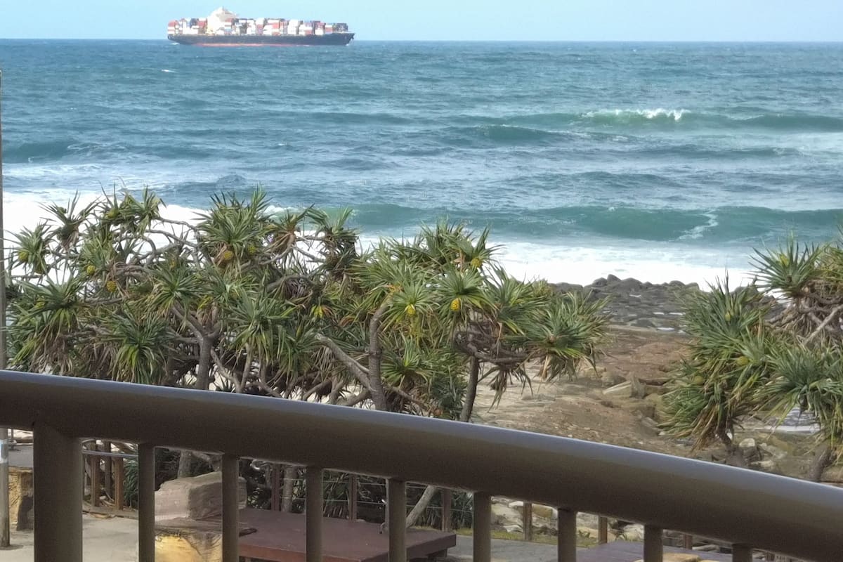 Vista costera con un barco a lo lejos, costa rocosa y vegetación tropical.