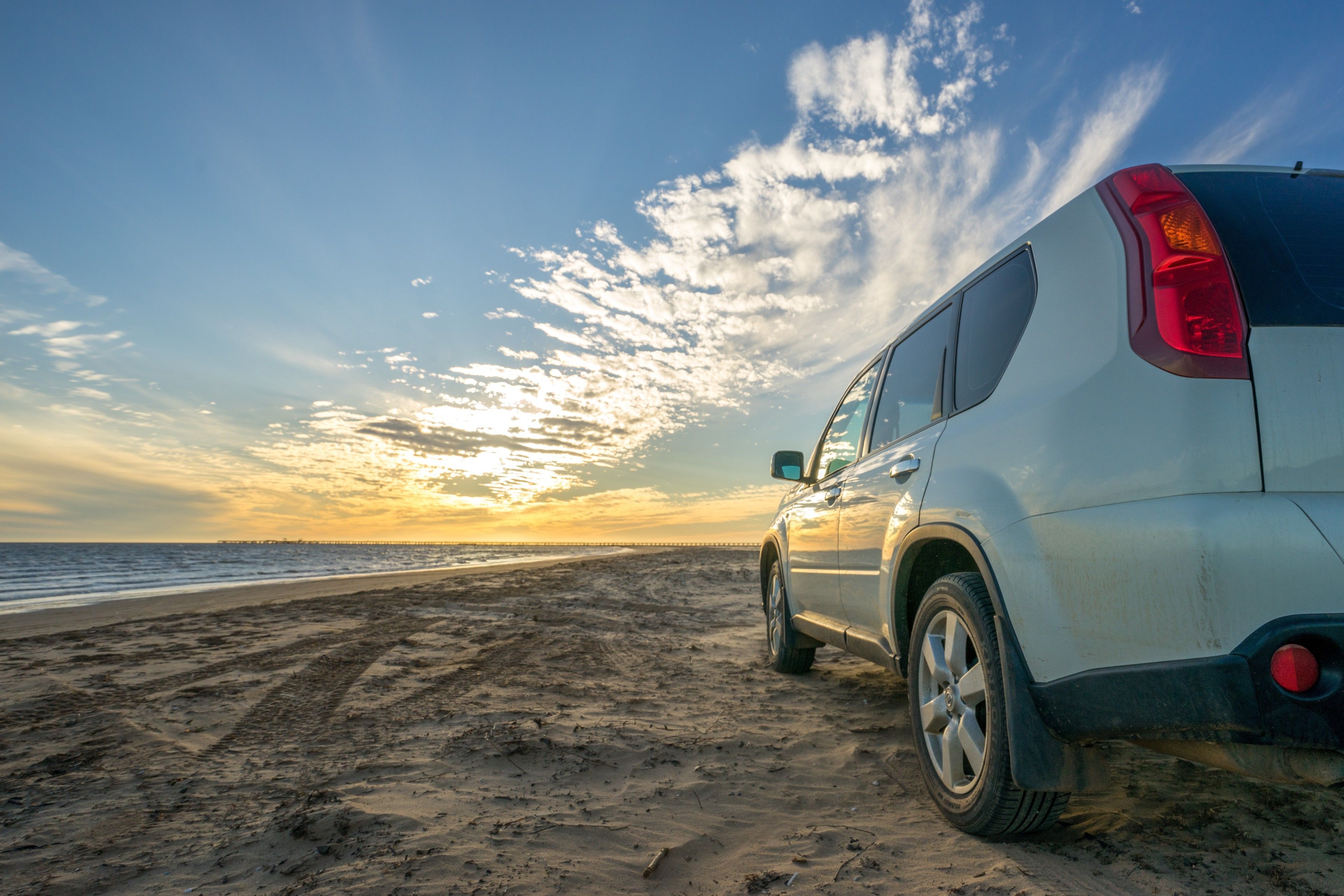 A white SUV parked on a sandy beach with a sunset in the background.