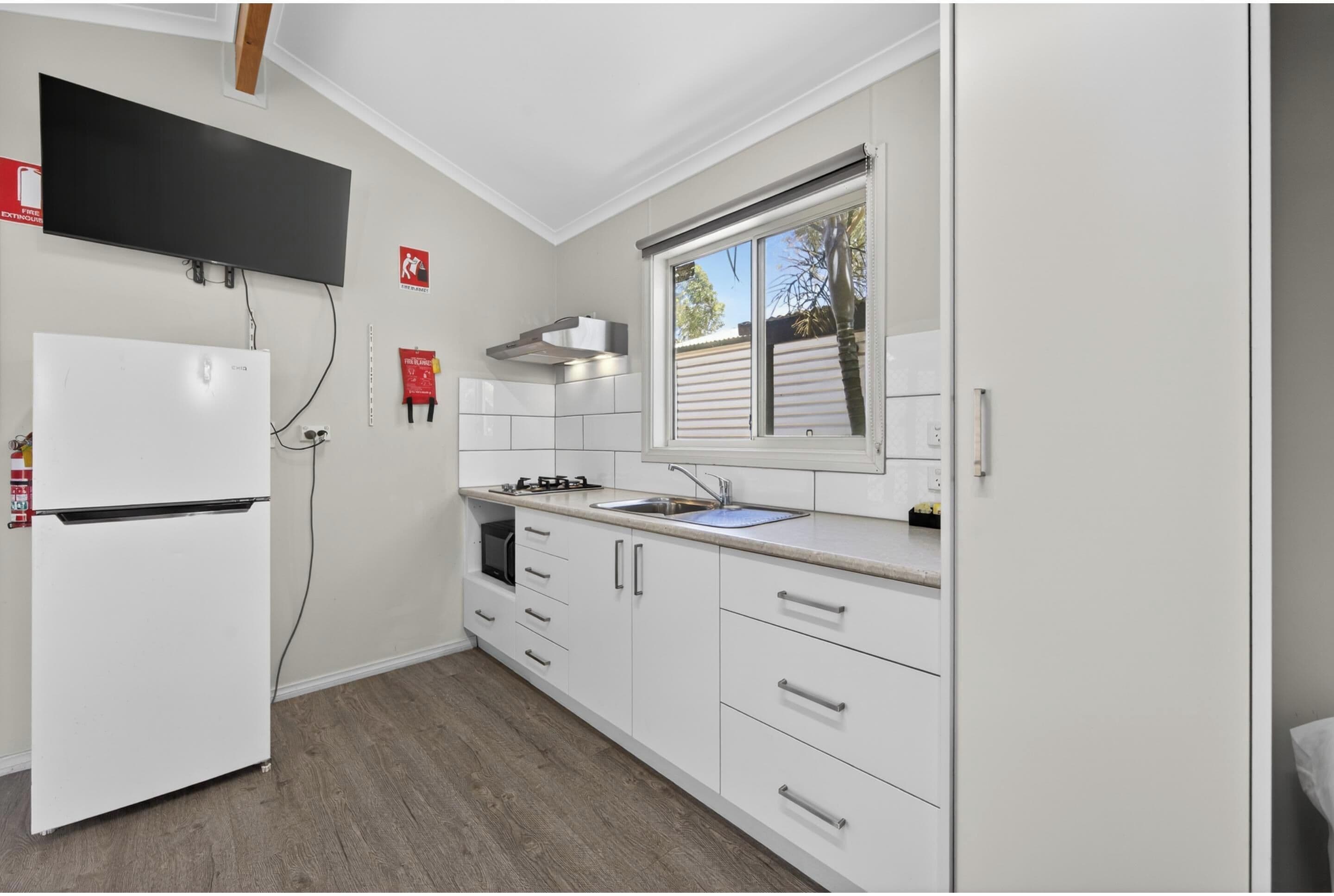 A modern kitchen with white cabinetry, a built-in oven, a stainless steel range hood, and a window with blinds.