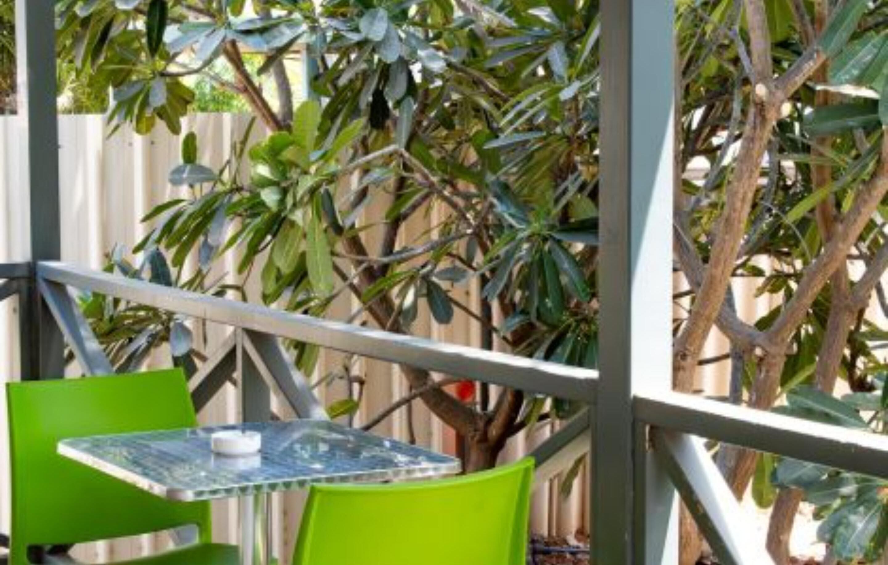 An outdoor seating area with a table and chairs, surrounded by a metal fence and greenery.