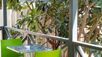 An outdoor seating area with a table and chairs, surrounded by a metal fence and greenery.