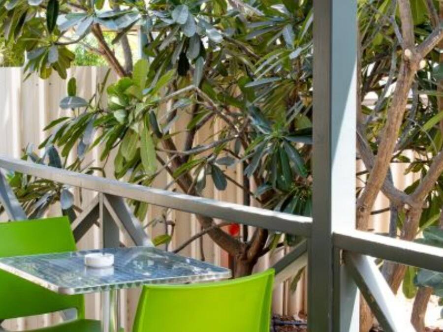 An outdoor seating area with a table and chairs, surrounded by a metal fence and greenery.