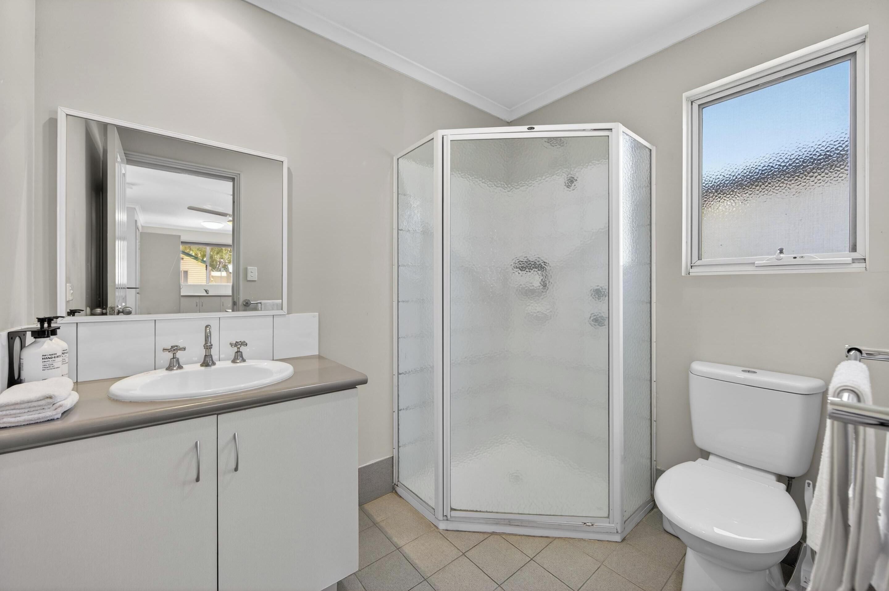 Un bagno moderno con doccia vetrata, lavandino bianco con due rubinetti e un water.