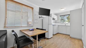 Una cocina moderna con zona de comedor, armarios blancos, televisor de pantalla plana y una ventana con persianas.
