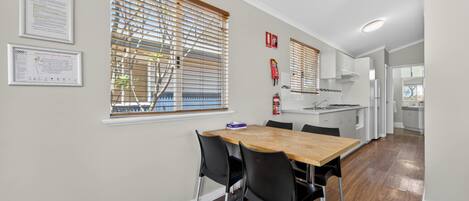 A modern kitchen with a wooden table and chairs, a window with blinds, and a fire extinguisher on the wall.