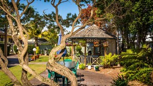 A gazebo with a tiled roof, surrounded by lush greenery and a brick pathway.