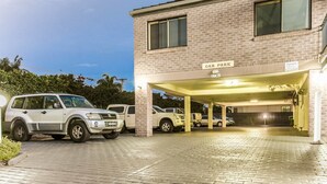A car park with a brick building, a covered area, and several parked vehicles.
