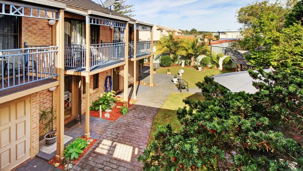 A two-story residential building with a balcony, brick exterior, and a well-maintained garden.
