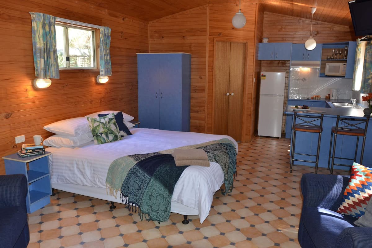 Una cabaña acogedora de madera con una cama, un pequeño rincón de cocina y un comedor.