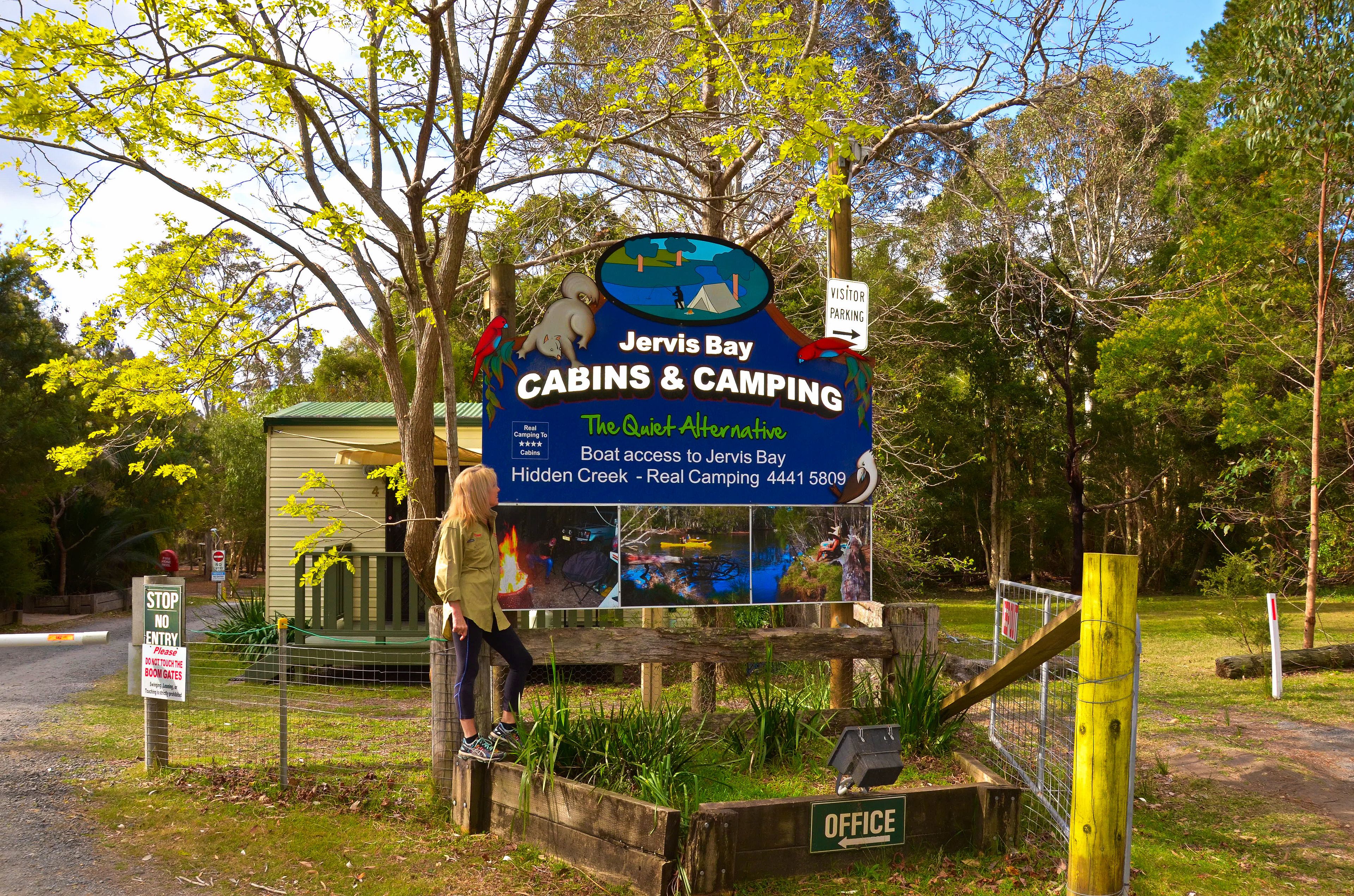 A sign for Jervis Bay Cabins & Camping with a view of the surrounding area.
