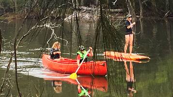 Ein rotes Kanu auf ruhigem Wasser, eine Person paddelt und eine andere steht an einem Steg.