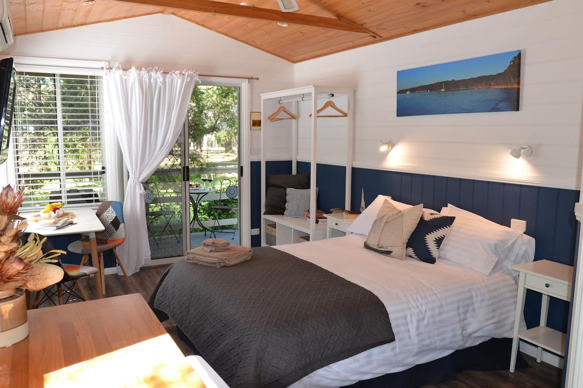 Un dormitorio con cama, mesitas de noche, un escritorio con silla y una ventana con cortinas.