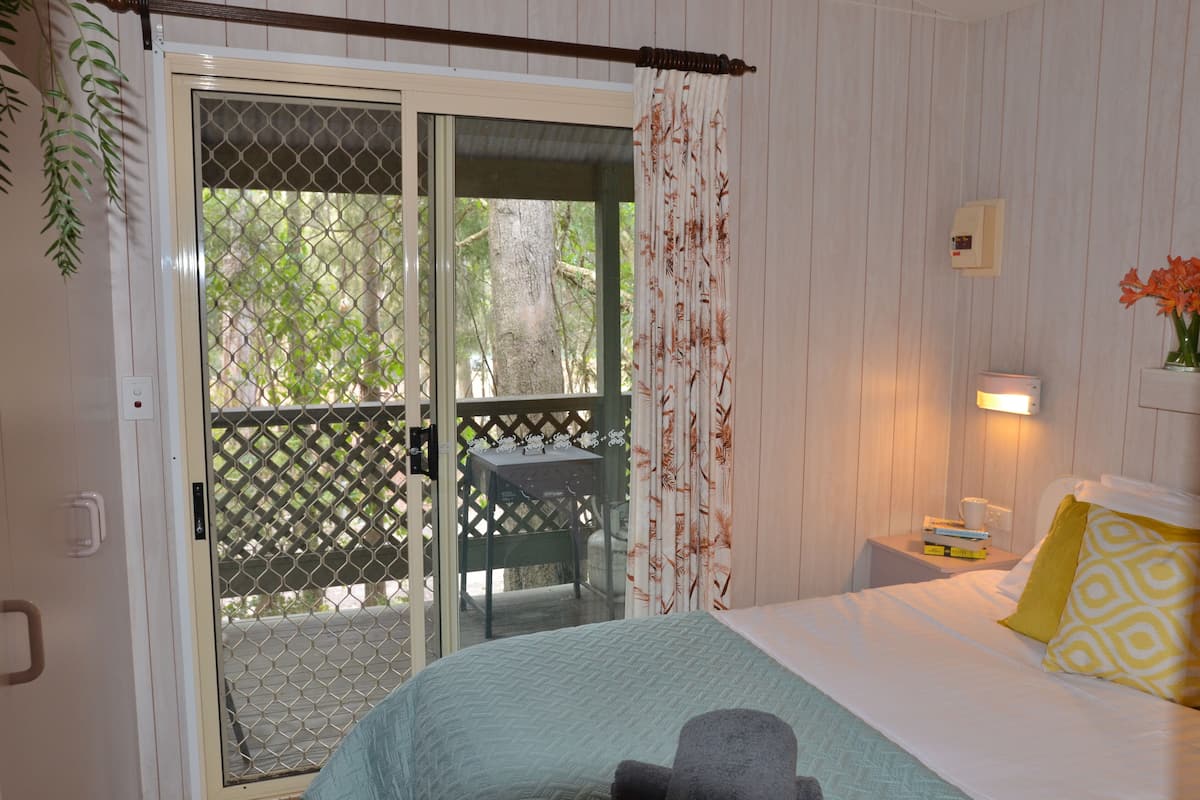 Un dormitorio con cama, mesita de noche, lámpara y vistas a un balcón con mesa y sillas.